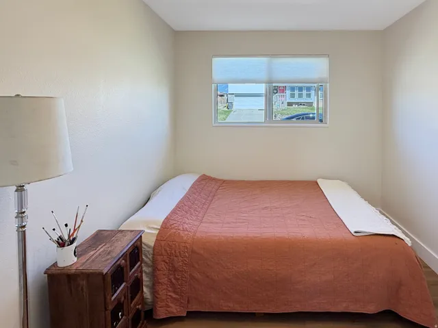 Bedroom featuring light-toned walls, wood-finish flooring, and a single window with blinds