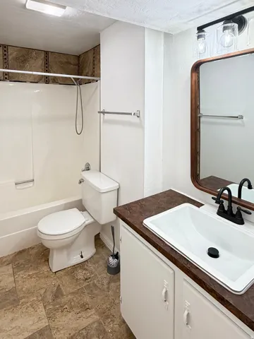 Bathroom featuring a white bathtub, ceramic tile shower surround, brown-toned floor tiling, and a vanity with a white sink and dark countertop