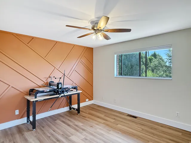 Room featuring a decorative accent wall with geometric paneling, wood-finish flooring, and crisp white baseboards