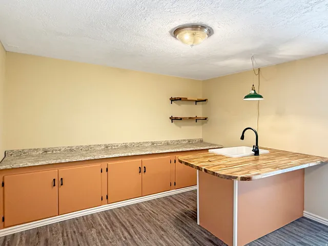 Utility room featuring a wood-finish flooring, built-in lower cabinetry with granite-look countertops, an island with butcher block countertop and integrated sink, and open shelving