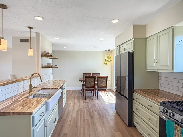 Spacious kitchen featuring light green cabinetry with wood-finish countertops, a farmhouse sink, and a stainless steel appliance suite