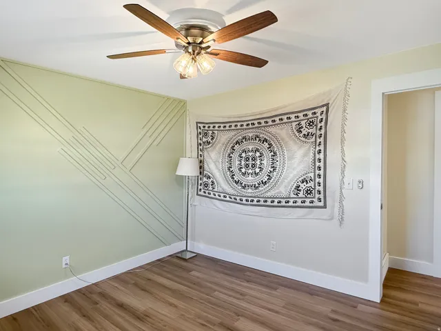 Light green accent wall with geometric molding, wood-finish flooring, white baseboards, and a ceiling fan with light fixture
