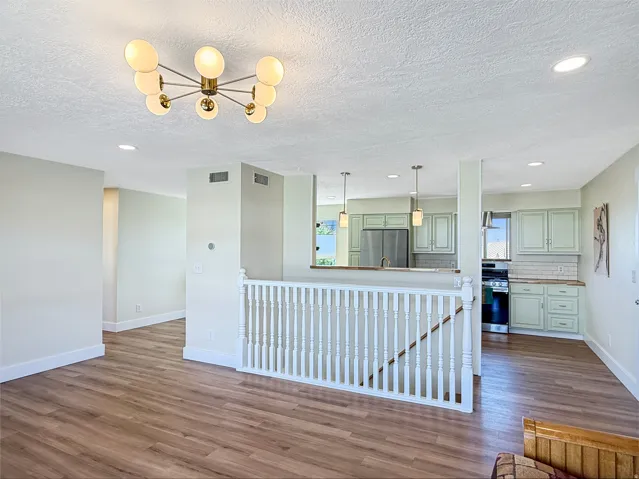 Open concept living area featuring wood-finish flooring, a contemporary ceiling light fixture, recessed lighting, and a white baluster staircase