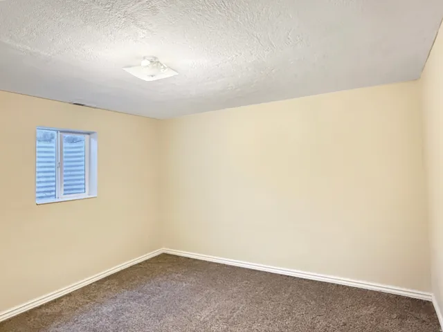 Room featuring light beige walls, a white-framed window with security bars, and brown patterned carpeting