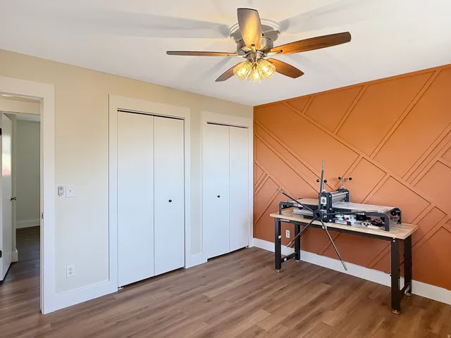 Interior room featuring a geometric accent wall in terra cotta, wood-finish flooring, and a ceiling fan with light fixture