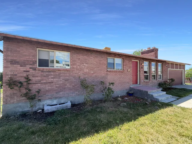 Brick exterior with a red front door, multiple front-facing windows, an attached garage, and a concrete front walkway