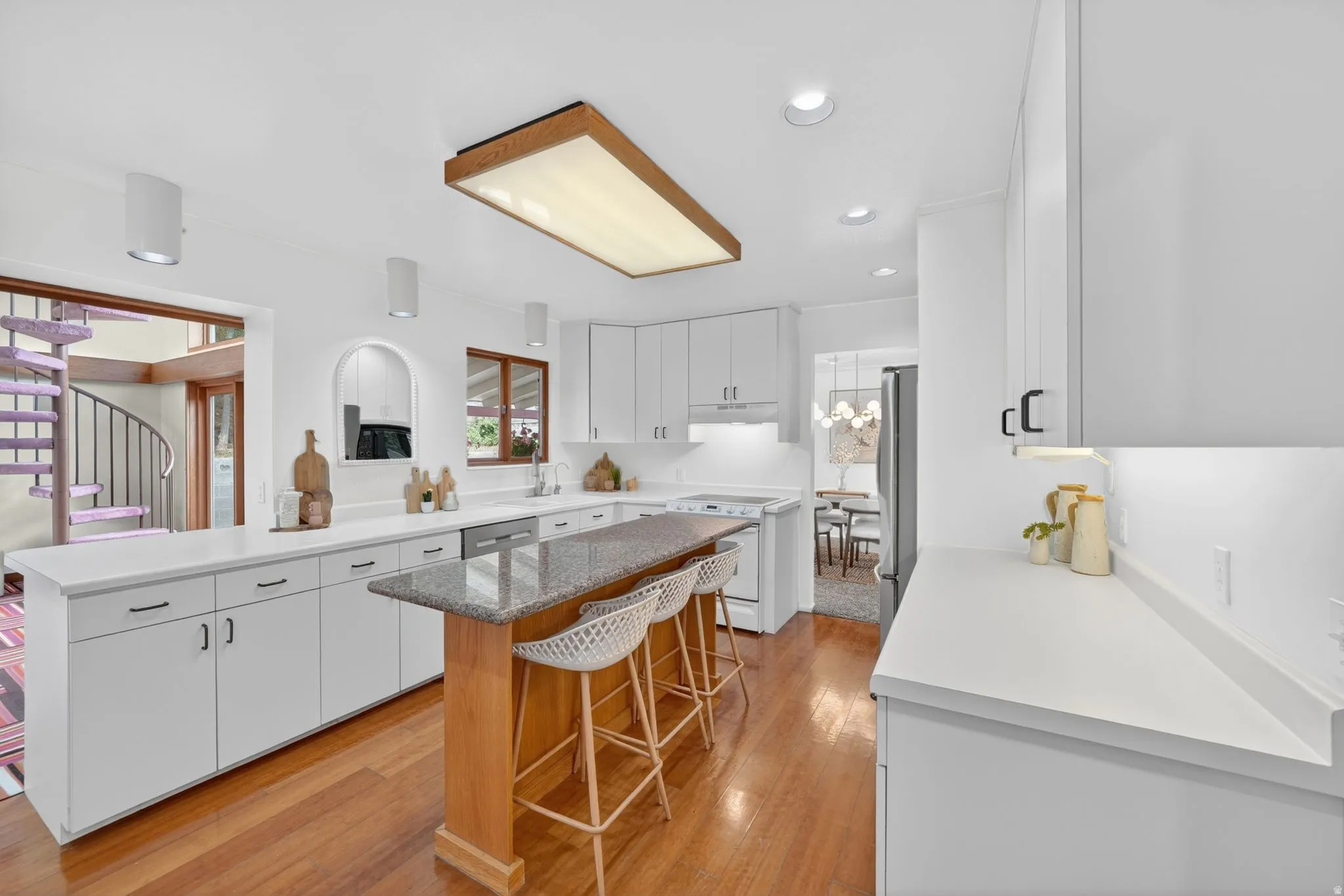 Bright kitchen featuring loads of white cabinetry, light countertops, a built-in electric range, and a breakfast bar