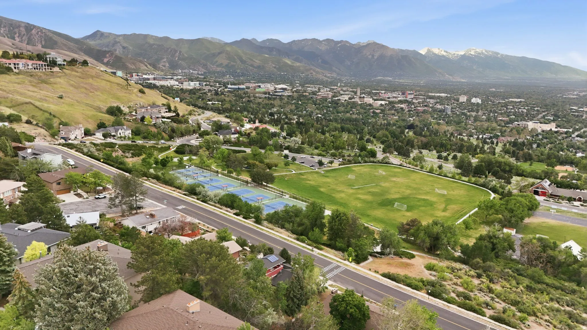 Expansive aerial perspective showcasing a mountainous backdrop, a verdant park with sports fields, and residential properties