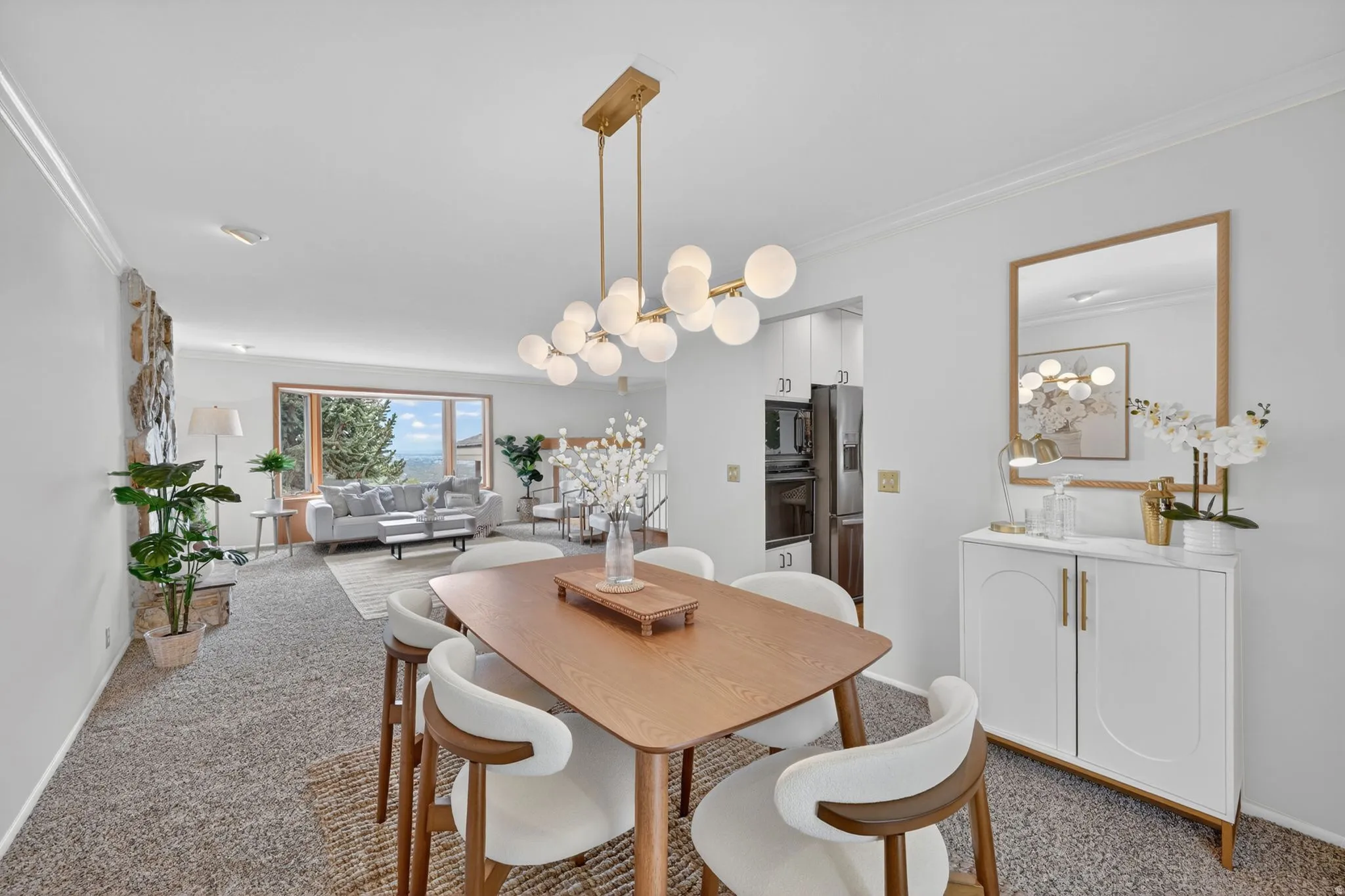 Open-concept dining and living areas featuring a modern linear chandelier, a stone-clad fireplace wall, large picture windows, recessed lighting, and crown molding