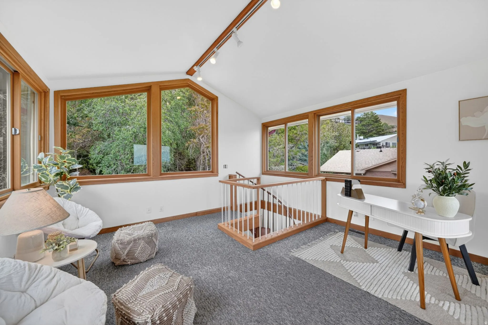 Loft space featuring extensive wood-framed windows, sloped ceiling with recessed track lighting, and grey carpet flooring
