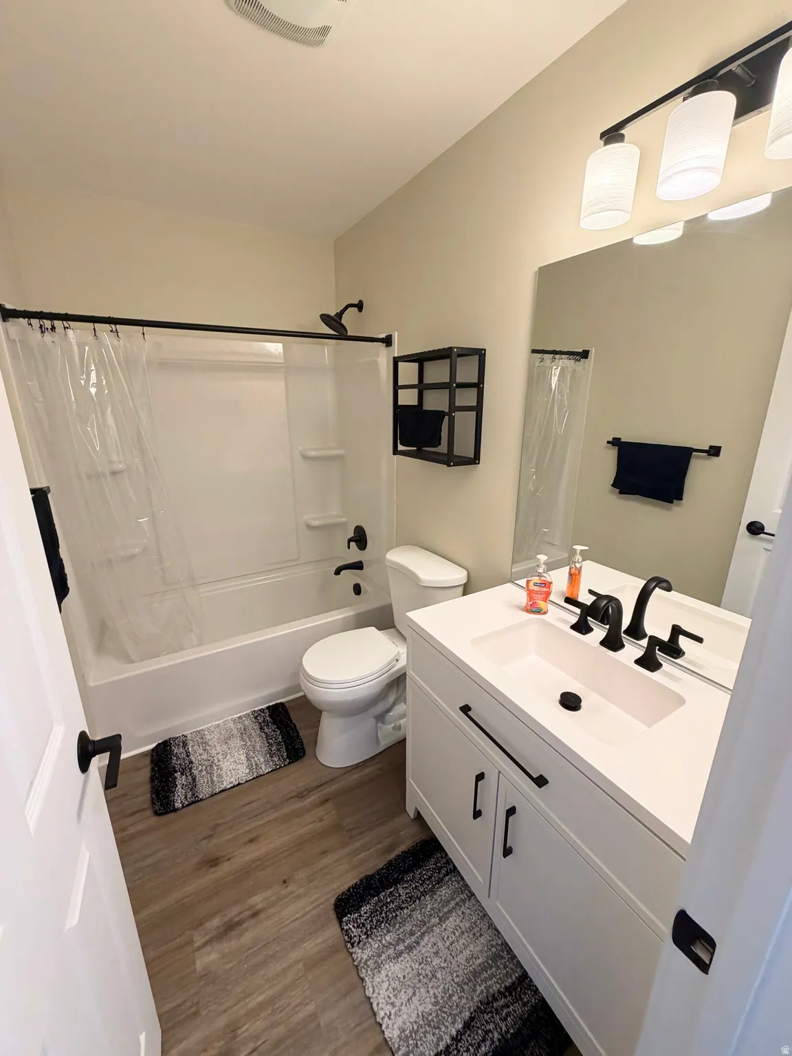 Bathroom featuring a white vanity with integrated sink, matte black fixtures, wood-finish flooring, a white bathtub with shower, and a frameless mirror