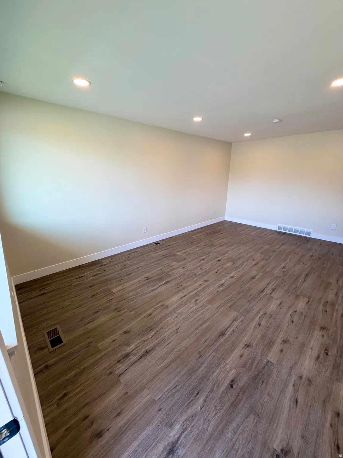 Spacious room featuring wood-finish flooring, recessed lighting, neutral paint, and white baseboards