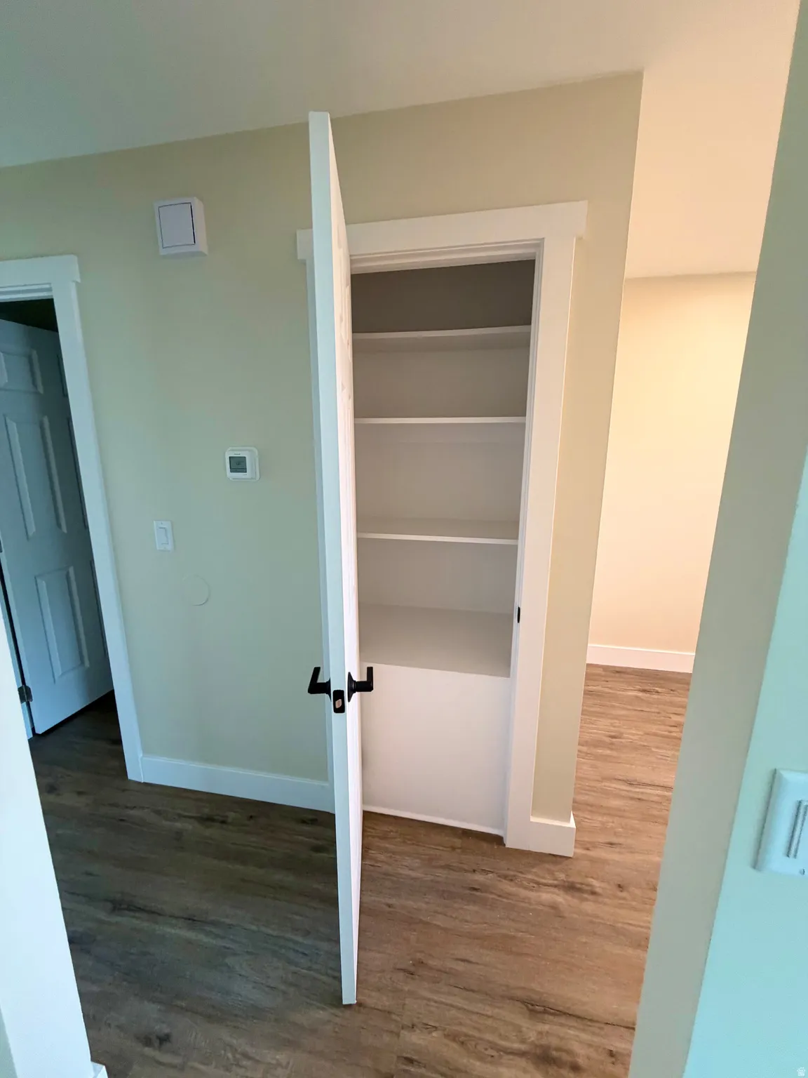 Recessed closet with multiple white shelving units and a lower cabinet space