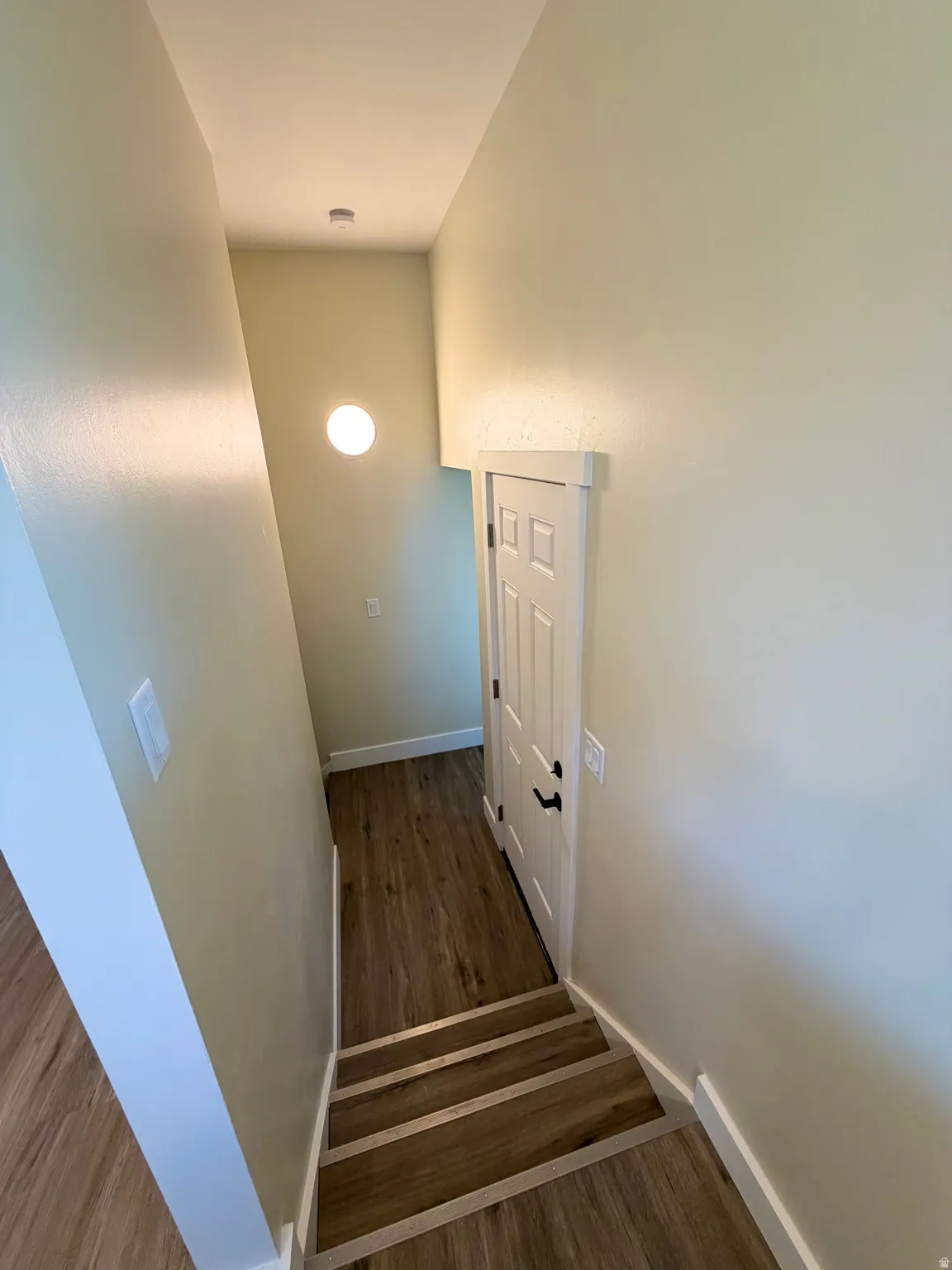 Stairwell with wood-finish flooring, white trim, and a contemporary wall-mounted light fixture