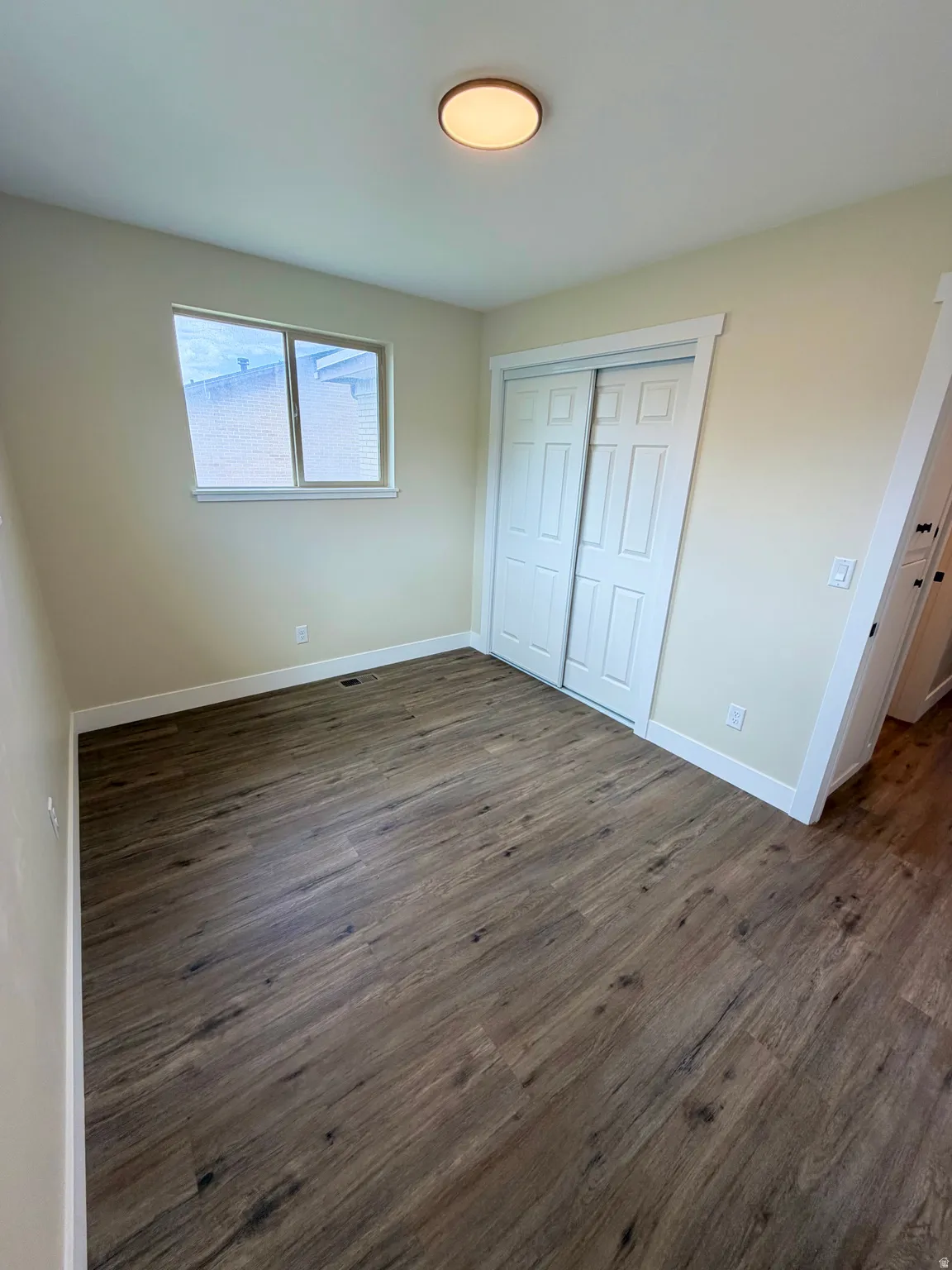 Room featuring wood-finish flooring, a double-door closet, a single window, and a flush mount ceiling light fixture
