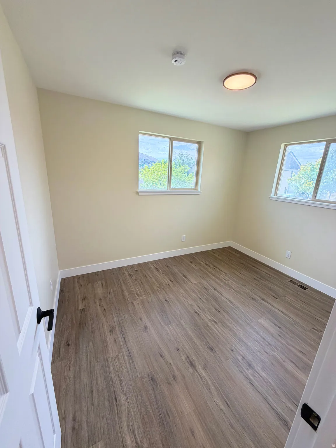 Room featuring wood-finish flooring, white baseboards, and two windows