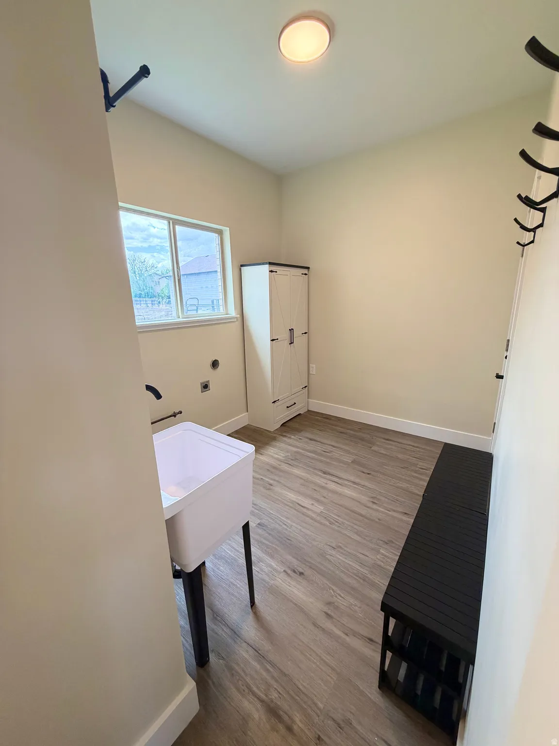 Laundry area with wood-finish flooring, a utility sink with a black wall-mounted faucet, and a window providing natural light