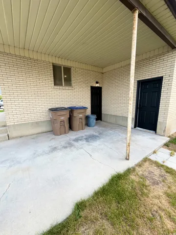 Covered concrete patio with light brick exterior, featuring two black doors and an exterior light fixture