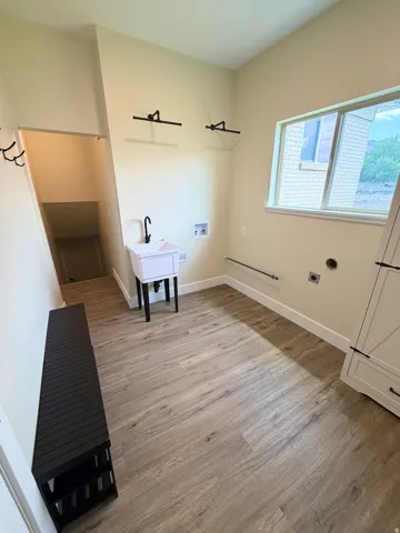 Spacious utility room featuring wood-finish flooring, a utility sink with a matte black faucet, and a large window providing natural light