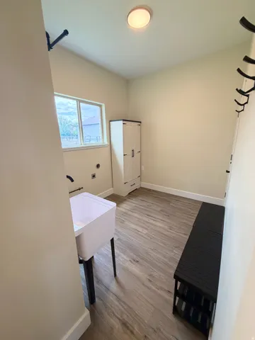 Laundry area with wood-finish flooring, a utility sink with a black wall-mounted faucet, and a window providing natural light