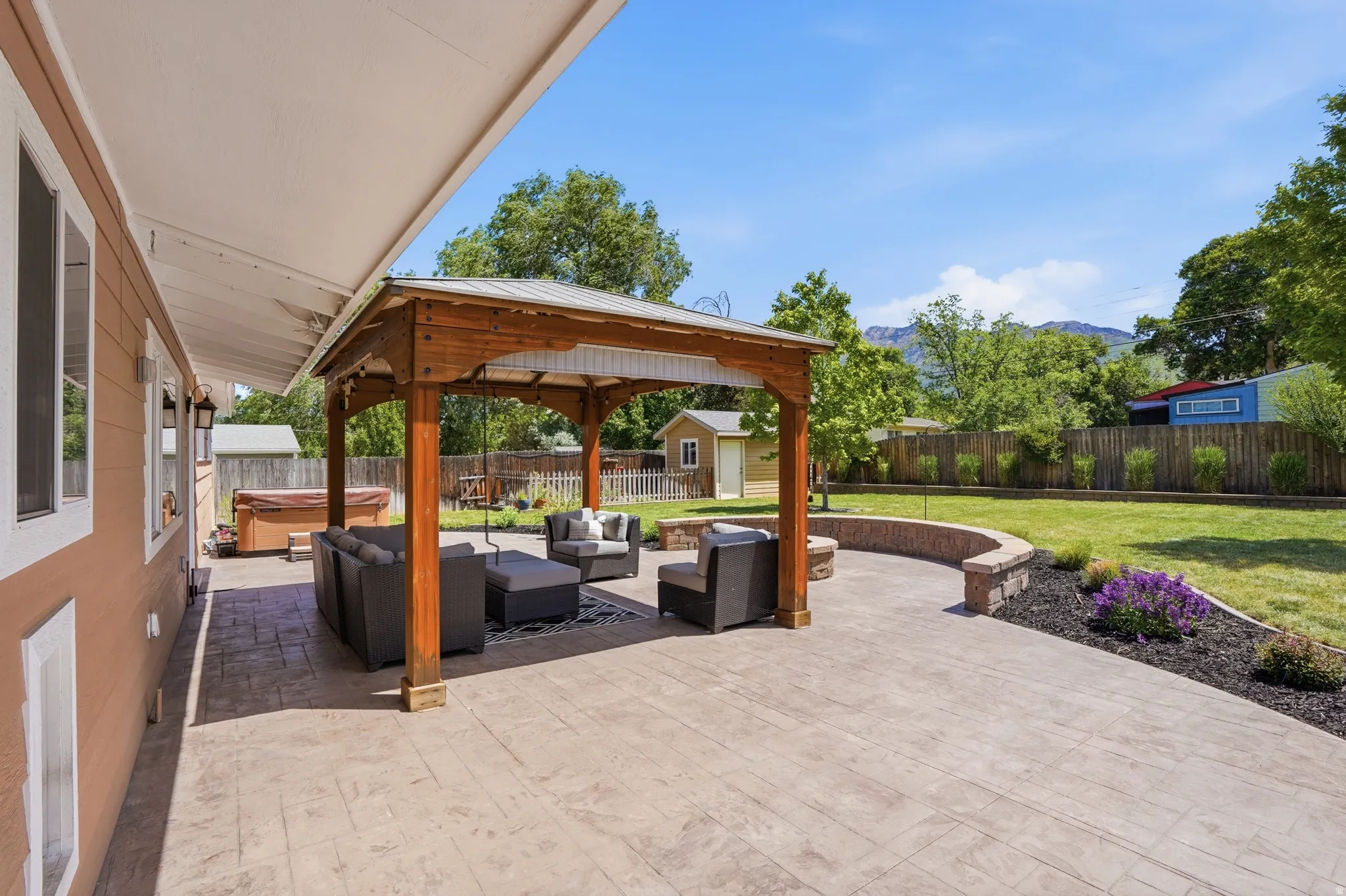 Expansive stamped concrete patio featuring a wood gazebo with a metal roof, a built-in stone retaining wall, and a fire pit