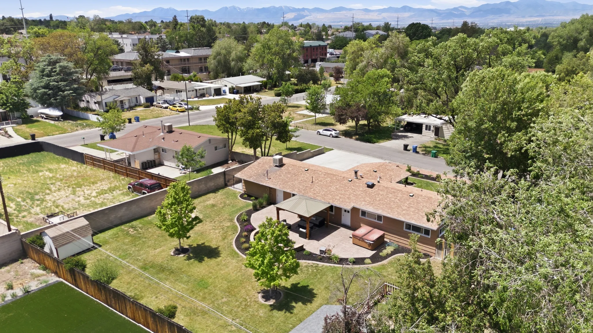 Expansive backyard featuring a manicured lawn, established trees, and a concrete patio with a covered outdoor area