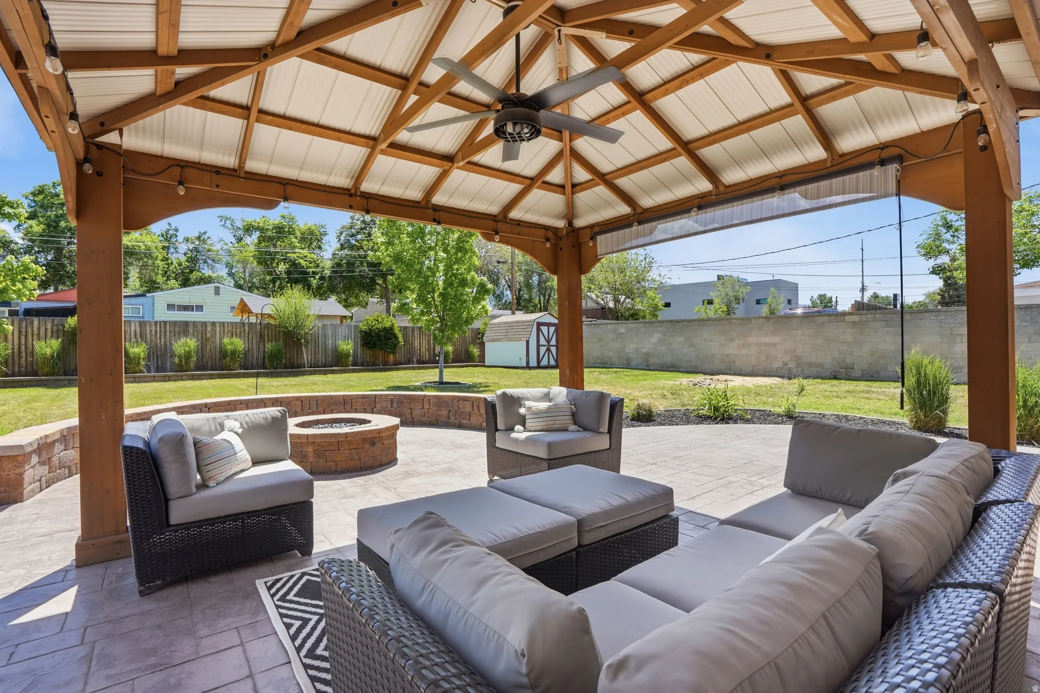 Expansive covered patio featuring a built-in ceiling fan, string lighting, Firepit, and stamped concrete flooring