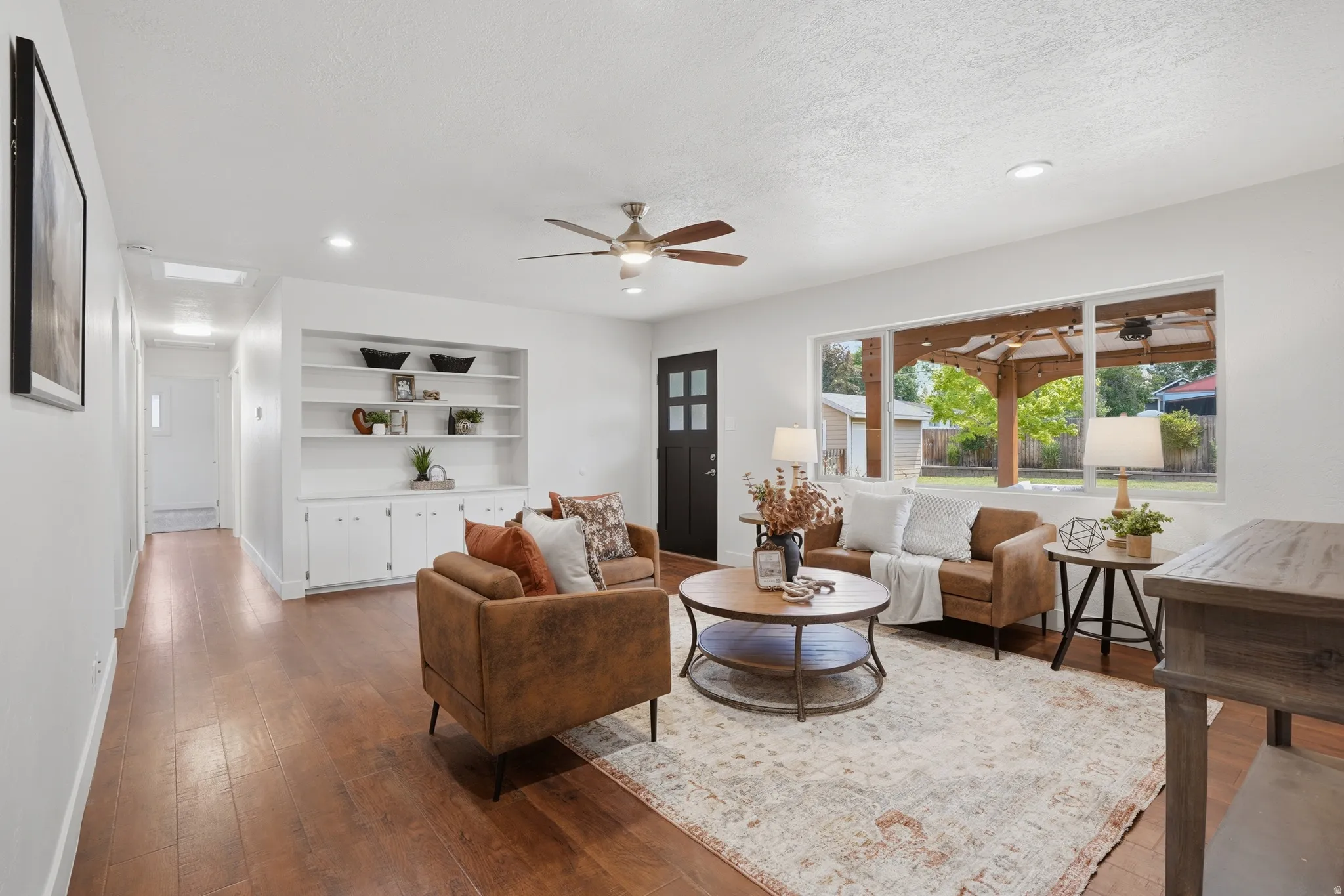 Spacious living area featuring wood-finish flooring, a ceiling fan, recessed lighting, and a large picture window