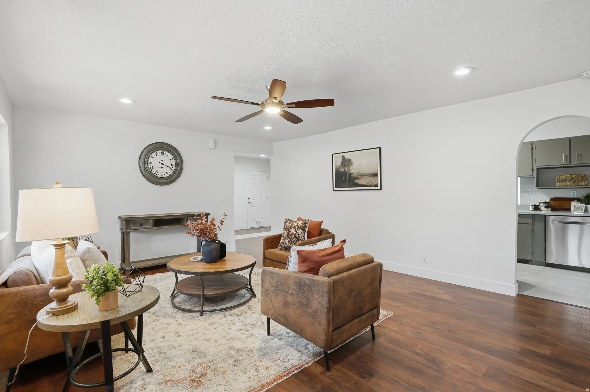 Spacious living area featuring wood-finish flooring, a ceiling fan, recessed lighting, kitchen entrance.