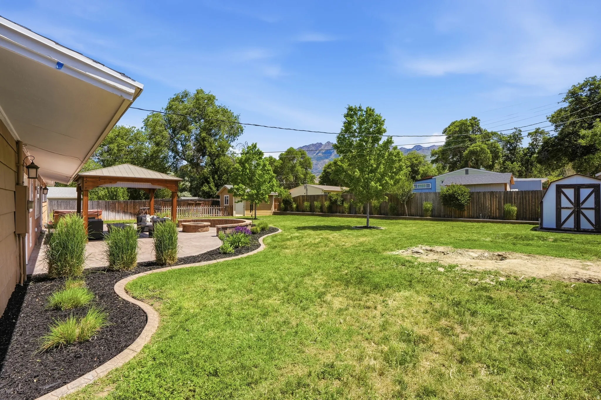 Expansive backyard featuring a large green lawn, a dedicated patio area, a wooden gazebo, a built-in fire pit, and a detached storage shed