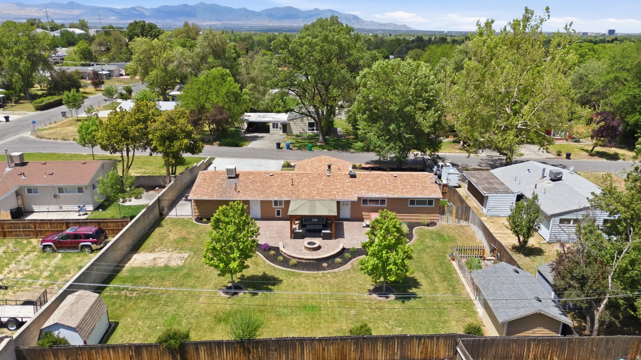 Expansive backyard featuring a stone patio, built-in fire pit, manicured lawn, and mature trees
