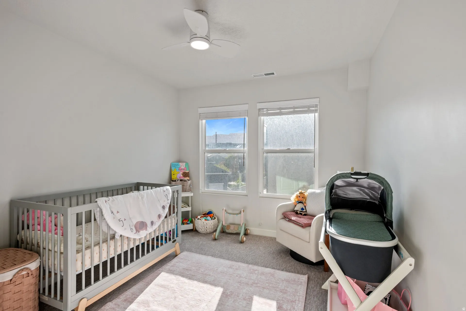 Room featuring twin windows, light gray walls, textured carpeting, and a ceiling fan with integrated lighting