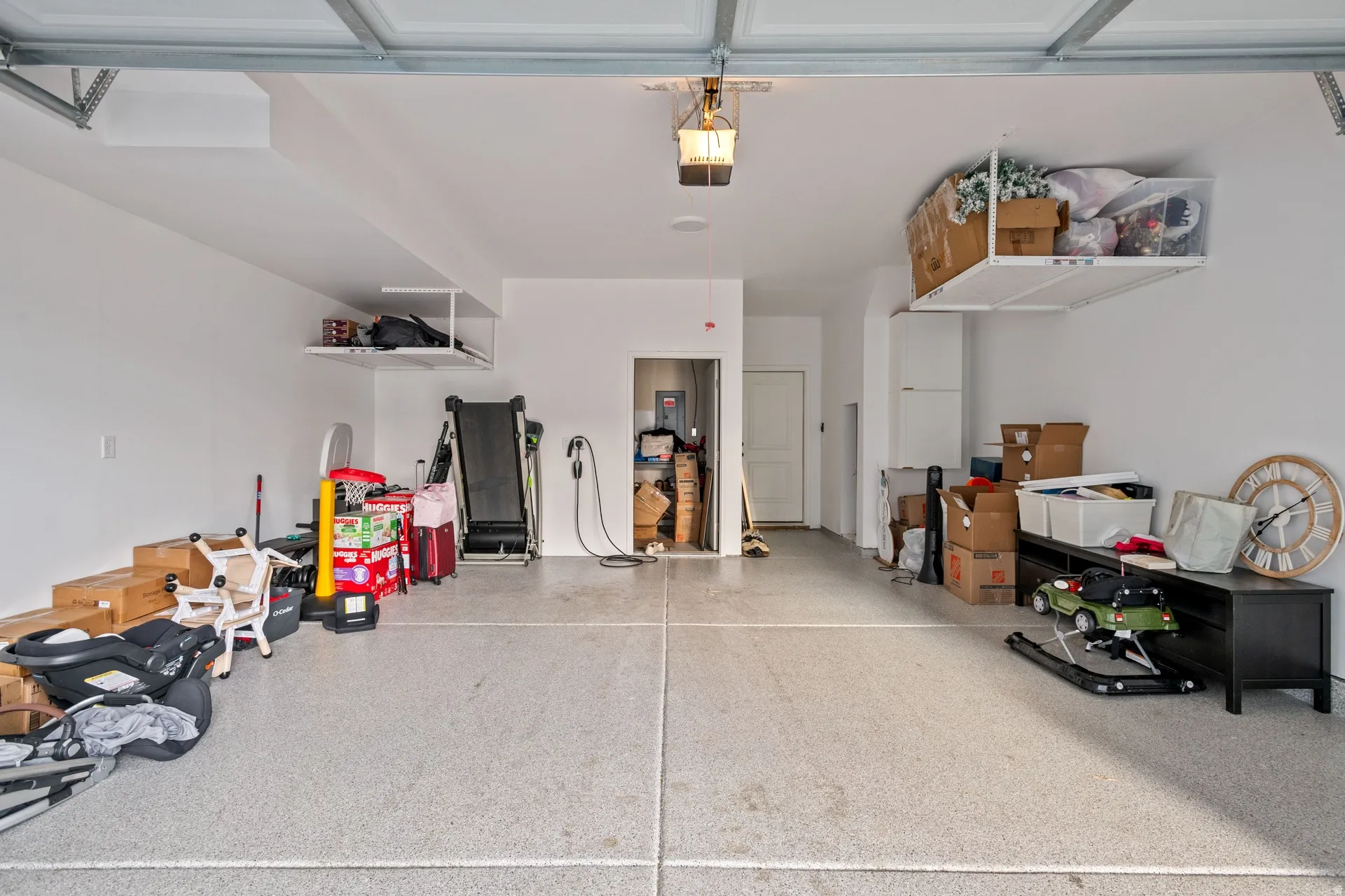 Spacious garage featuring a durable epoxy-coated concrete floor, two overhead storage racks, a wall-mounted EV charging station, and an interior access door
