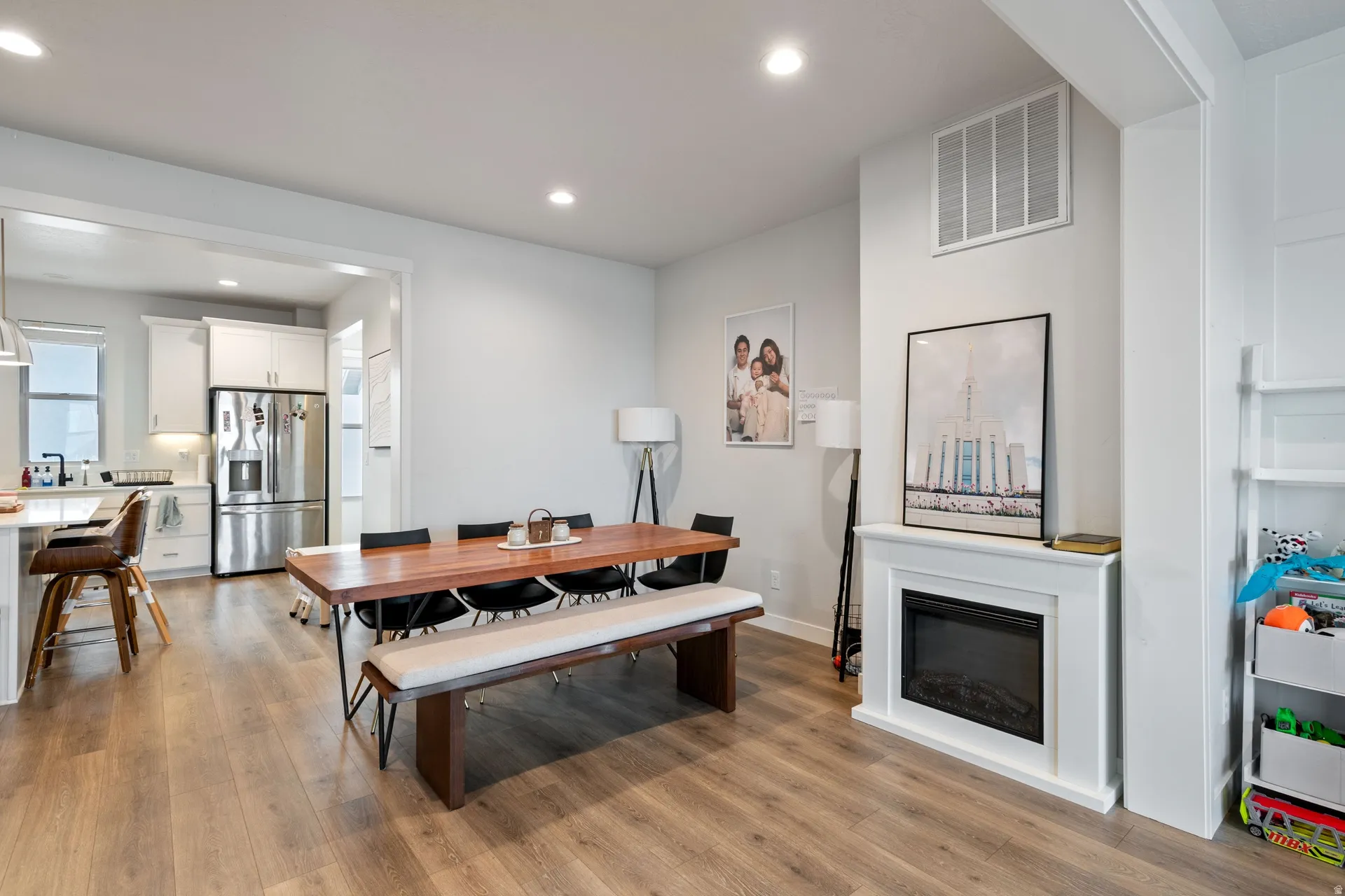 Open-concept dining area with wood-finish flooring, recessed lighting, and a white mantle fireplace