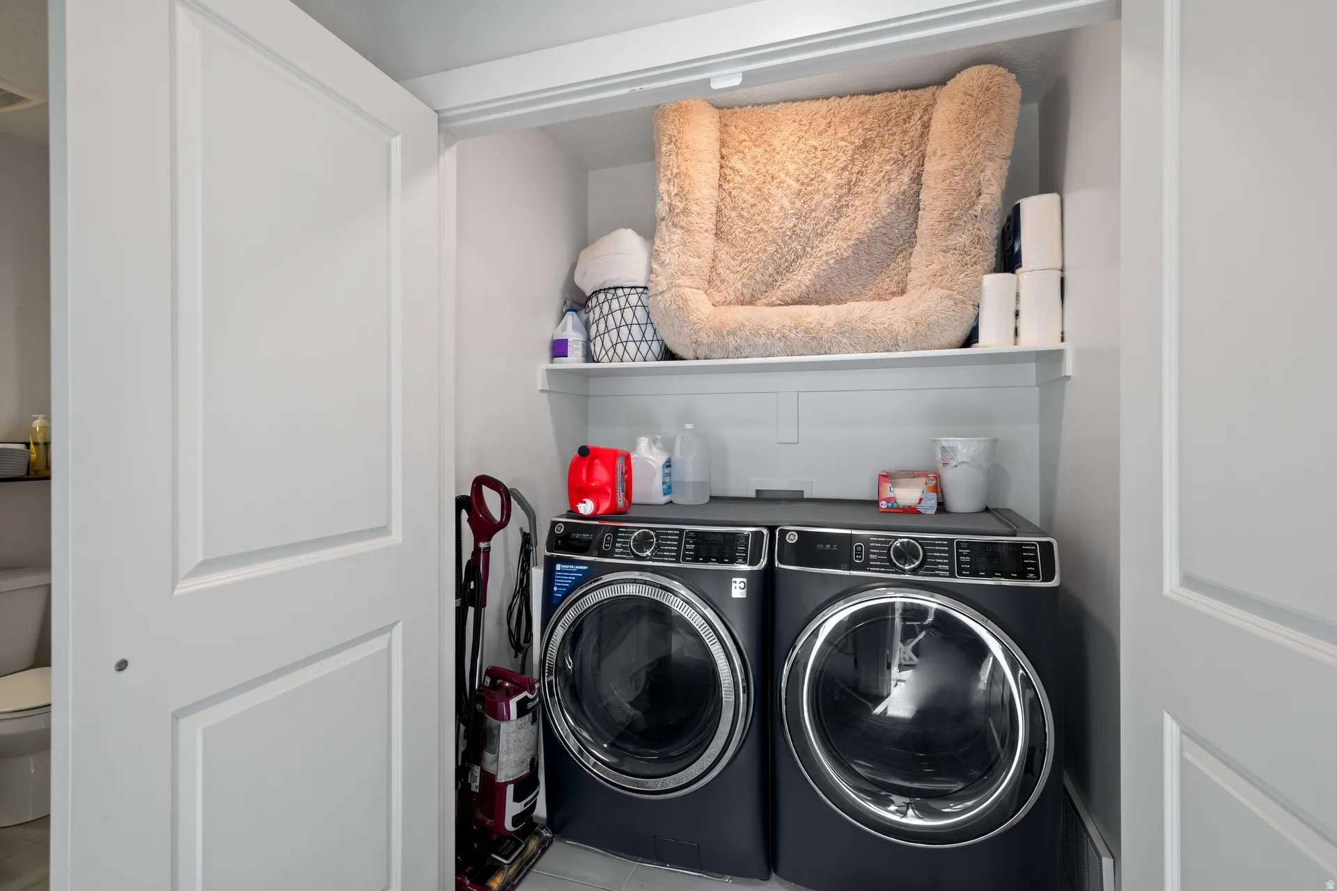 Dedicated laundry closet featuring a stacked washer and dryer, integrated shelving, and white paneled bi-fold doors