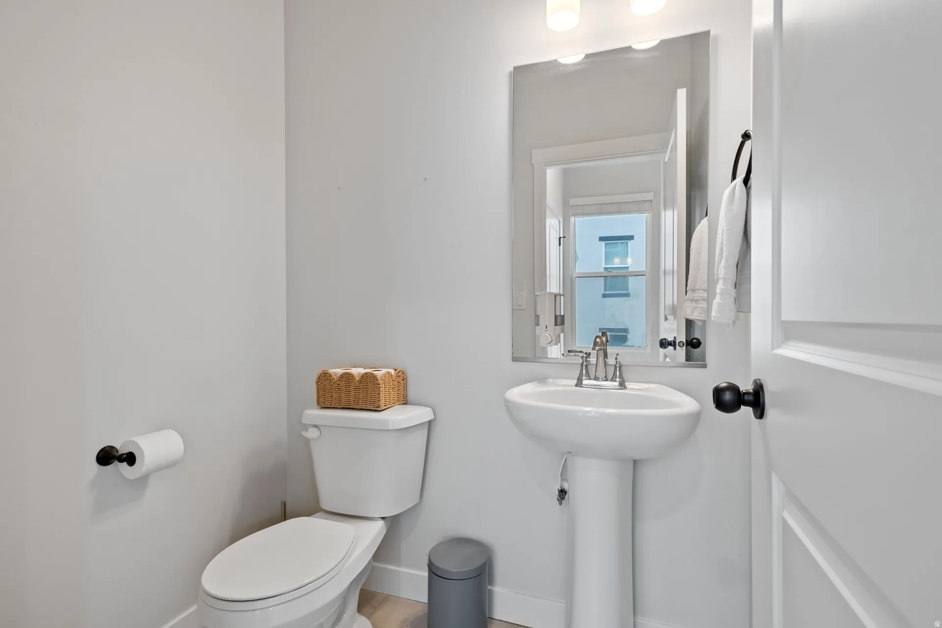 Pedestal sink with a brushed nickel faucet, framed by a rectangular mirror with sconce lighting