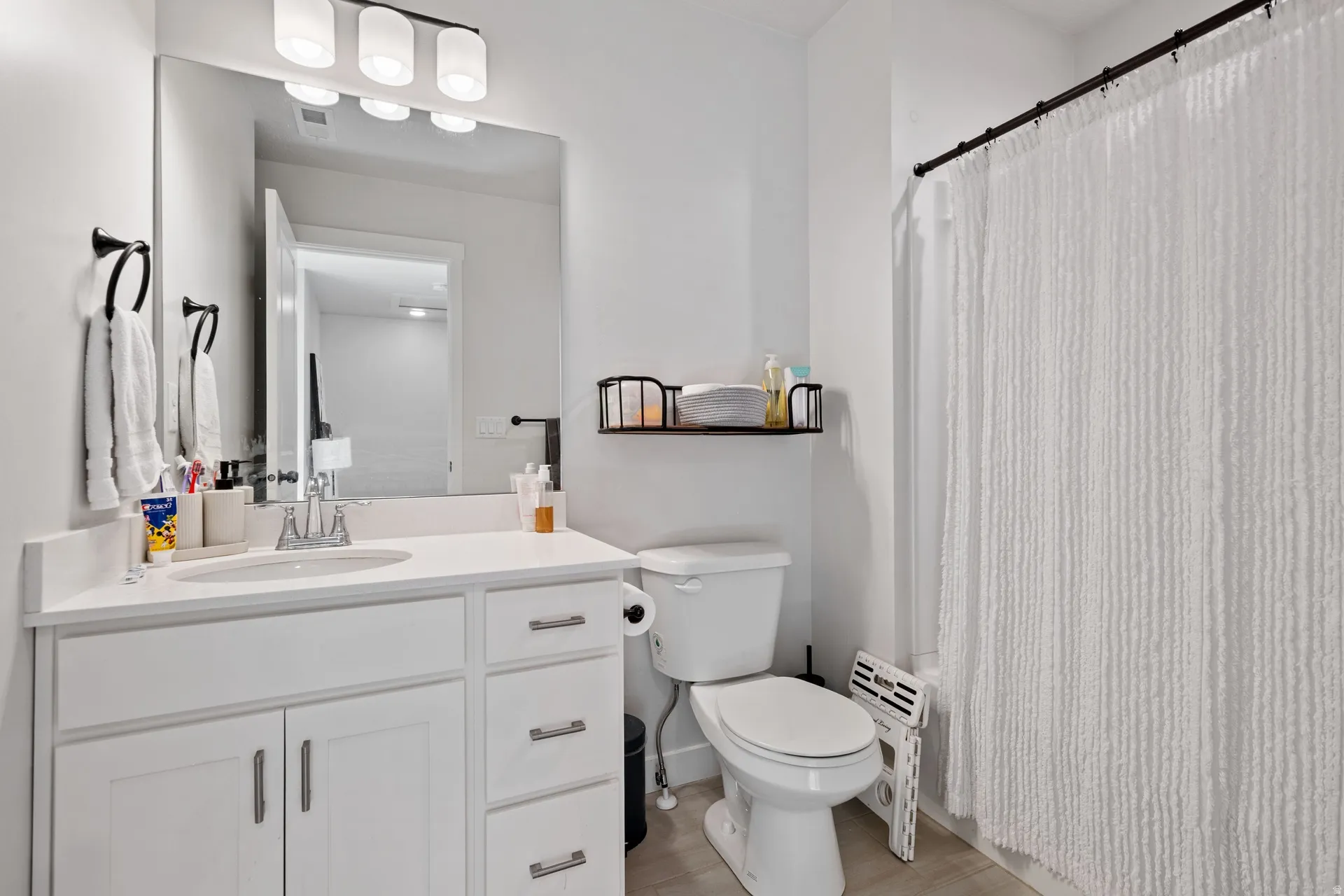 Bathroom featuring a white vanity with an integrated sink, a large wall-mounted mirror, a three-light fixture with opaque glass shades, and a white toilet