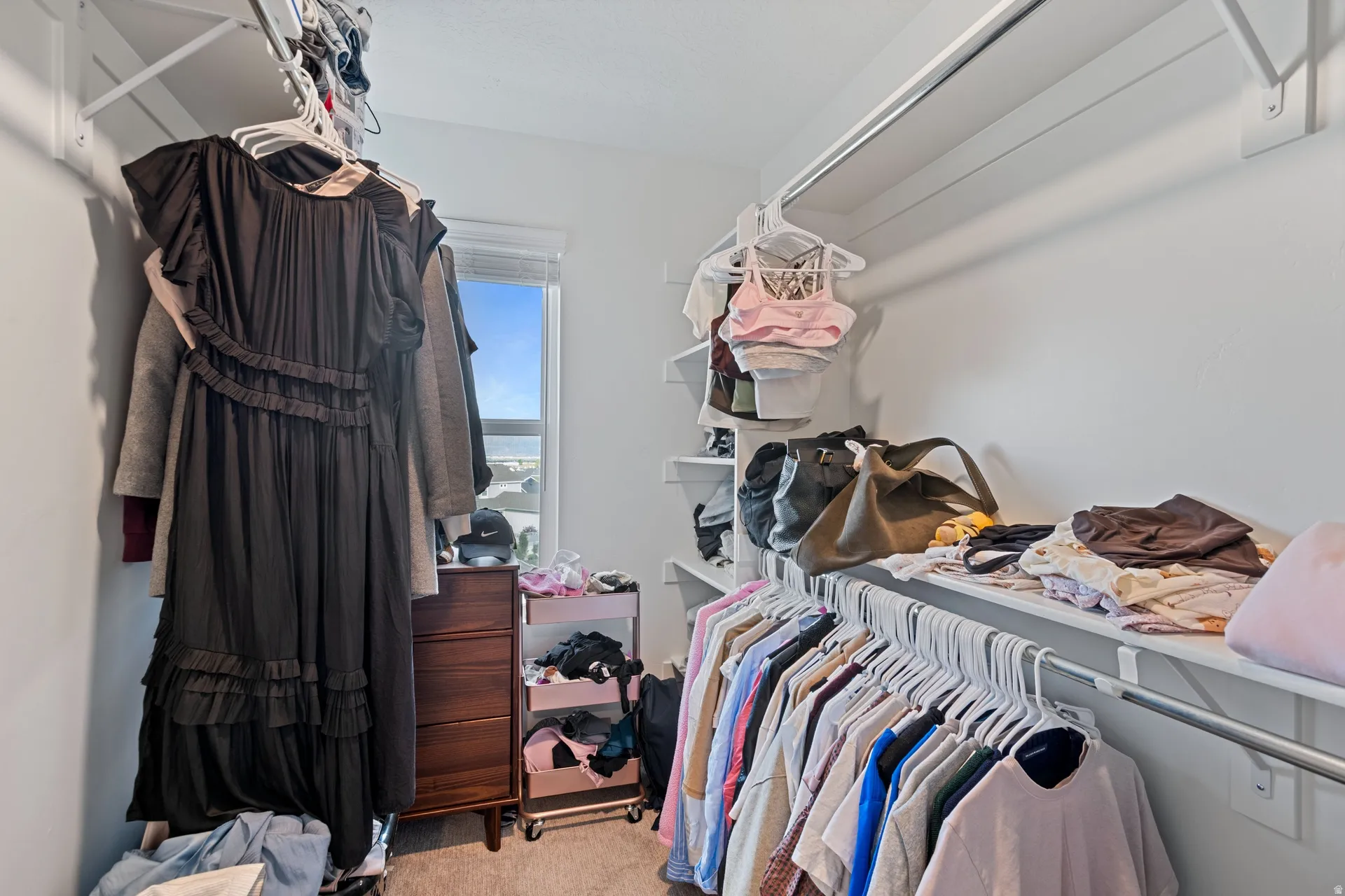Walk-in closet featuring white walls, ample built-in shelving, multiple hanging rods, and a window for natural light