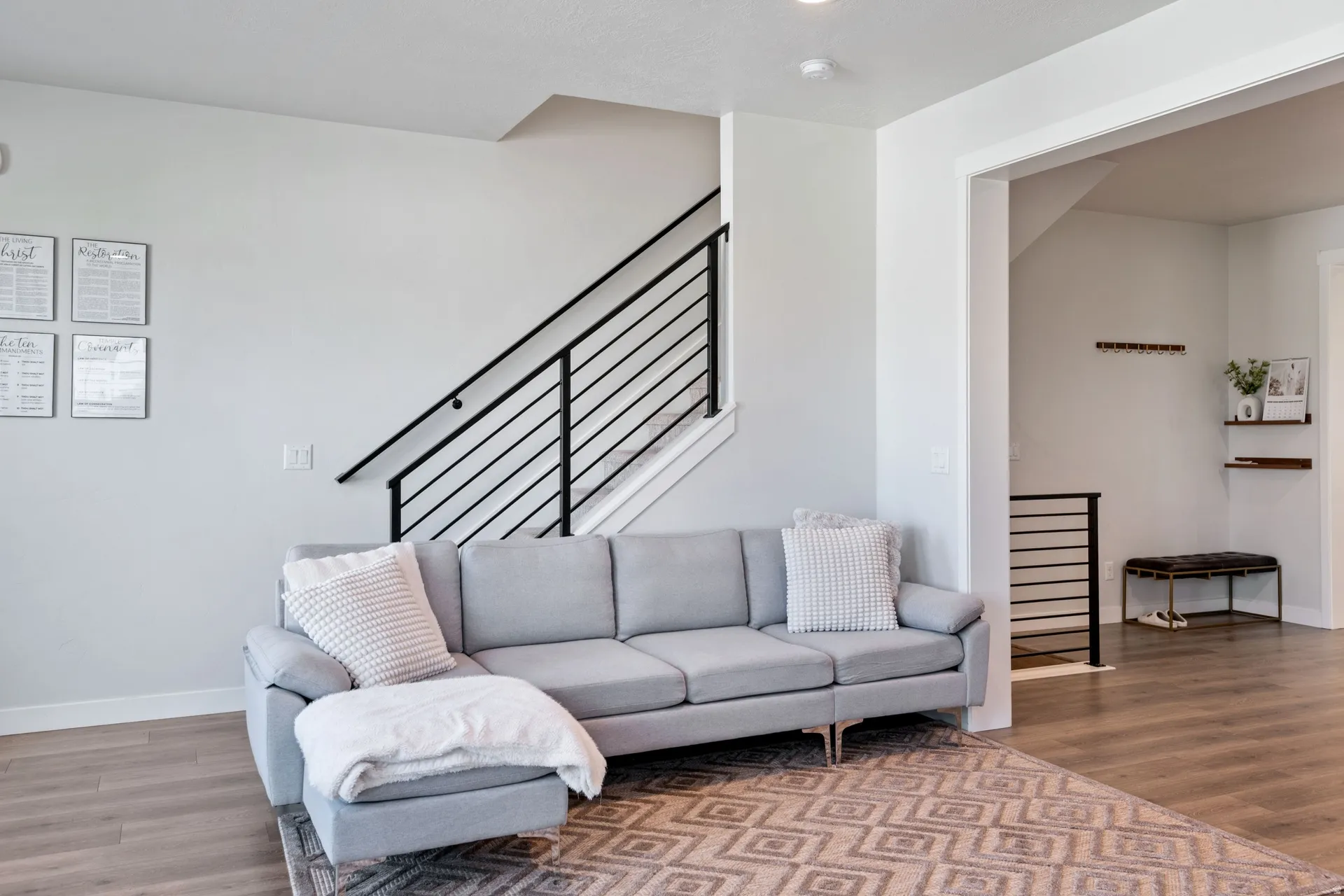 Open-concept interior featuring light gray walls, wood-finish flooring, a contemporary staircase with black horizontal railings, and recessed lighting