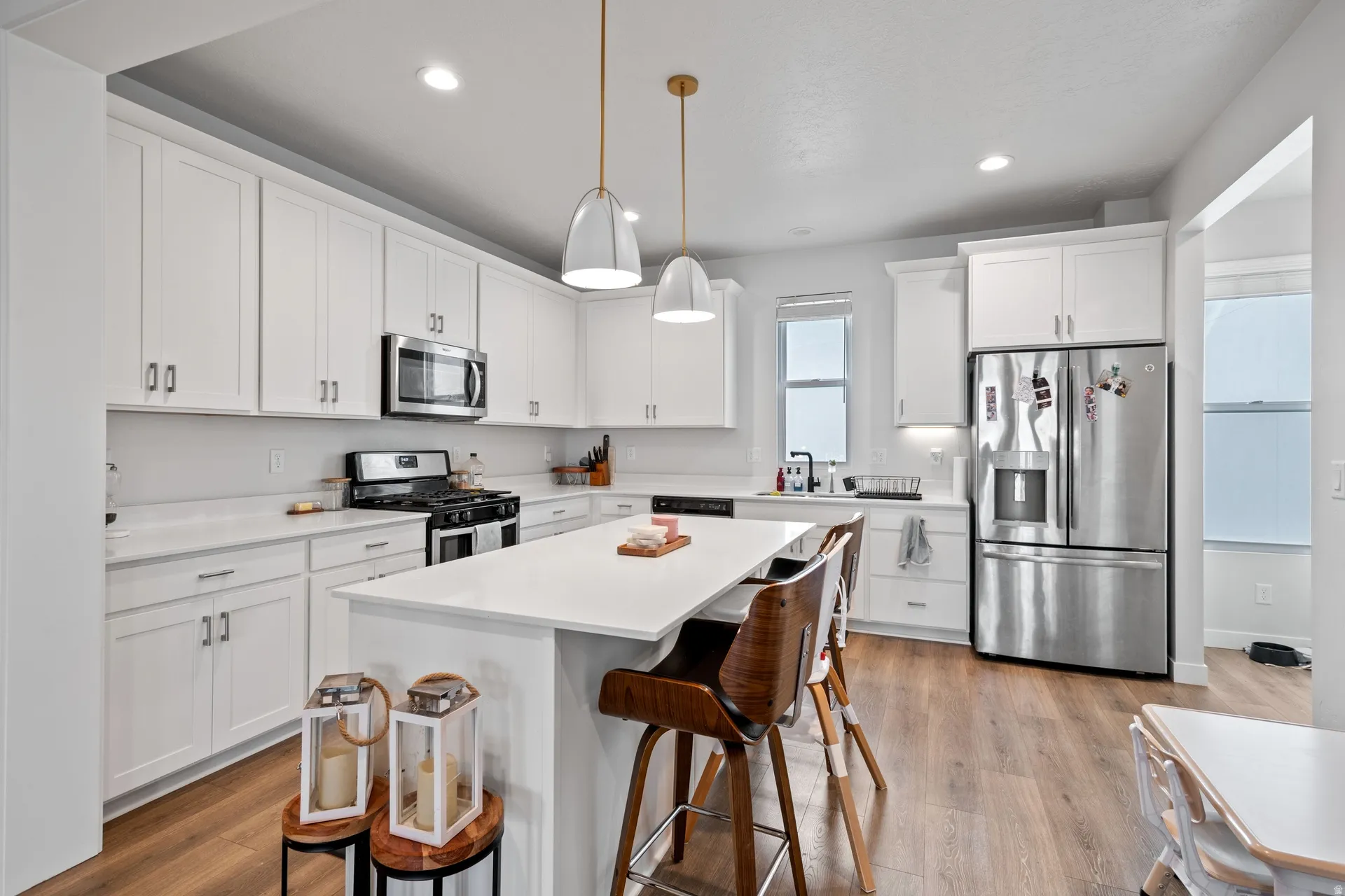 Modern kitchen featuring white shaker cabinetry, stainless steel appliances, a center island with countertop seating, recessed lighting, and wood-finish flooring