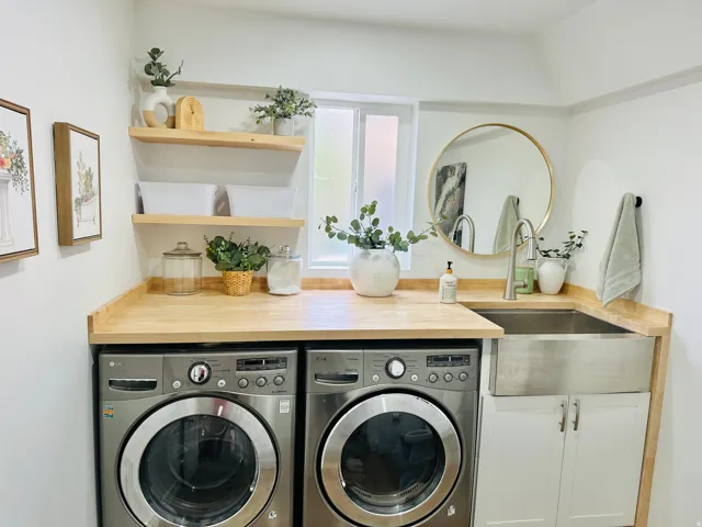 Dedicated laundry area featuring a wood-finish countertop, undermount stainless steel farmhouse sink with a brushed nickel faucet, and white base cabinetry