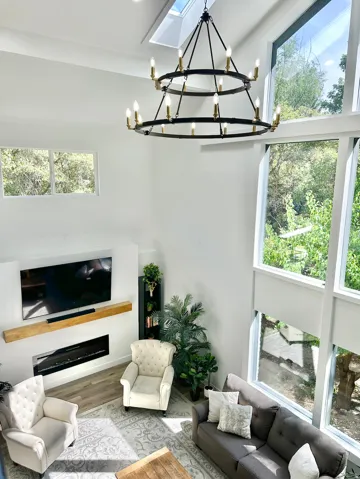 Two-story living area featuring a large two-tier chandelier, a wall-mounted linear fireplace with a wood mantel, and expansive floor-to-ceiling windows