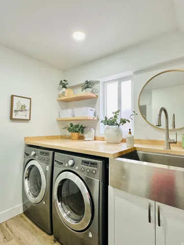 Laundry area featuring wood-finish countertops, a stainless steel apron front sink with a gooseneck faucet, white cabinetry, and wood-finish flooring