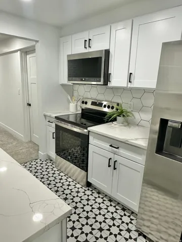 Kitchen featuring white shaker-style cabinetry, stainless steel appliances, a geometric tile backsplash, and patterned floor tiling