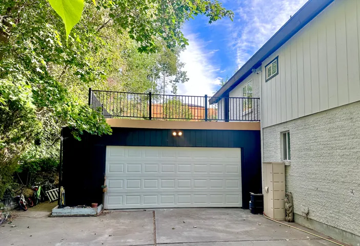 Exterior featuring a white garage door, black siding, and a second-story upper west deck with black railings