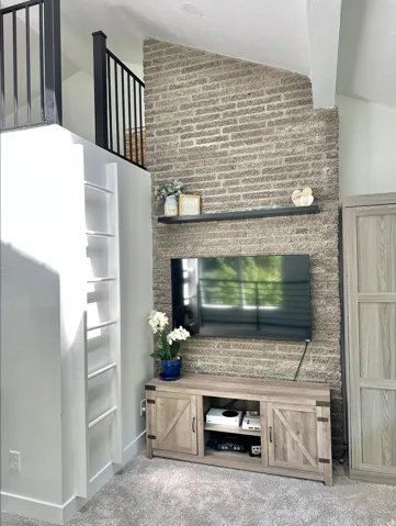 Floor-to-ceiling textured brick accent wall with a floating shelf. Ladder up to the upper loft.