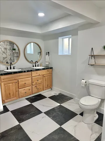 Dual vanity with light wood cabinetry and dark countertops