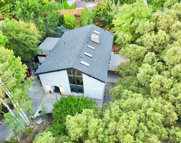 Contemporary residence featuring a dark shingled roof with multiple skylights, a light-toned exterior, and a prominent chimney
