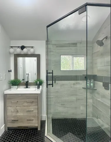 Bathroom featuring a frameless glass shower enclosure with matte black hardware, hexagon tile flooring, and a window