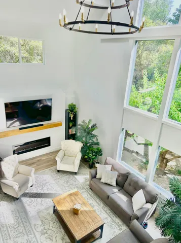 Two-story living area featuring a large chandelier, floor-to-ceiling windows, built-in fireplace, wood mantle, and wood-finish flooring